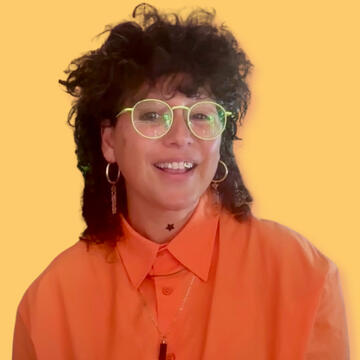 Jessica Lanyadoo color portrait. Jessica is wearing round light-colored glasses, a peach orange button-down, and has brown hair that is short in front and longer in the back, long, dangling earrings, and is smiling.