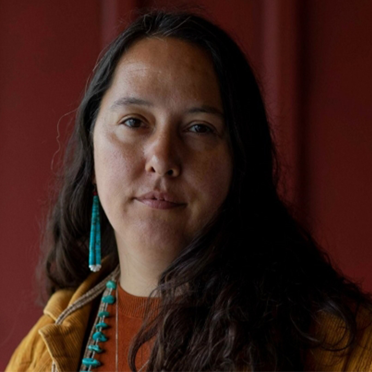 Rowen White color portrait. Rowen is from the Mohawk community of Akwesasne and is standing in a field of plants, and crops holding a woven basket in front of her and smiling.