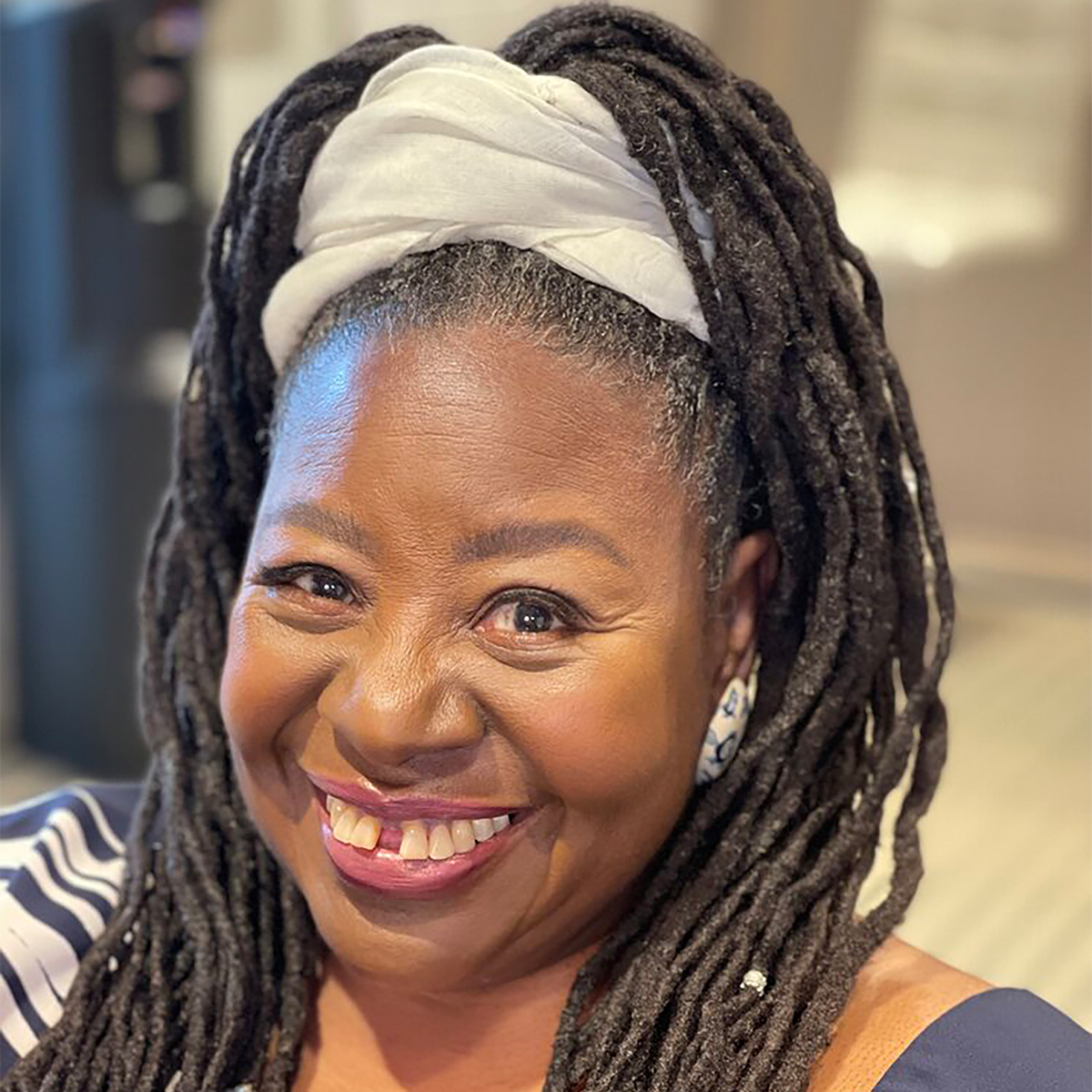 Loretta Ross black and white portrait. Loretta is a Black woman who is smiling and her her braided Black and silver hair tied up with a white wrap.