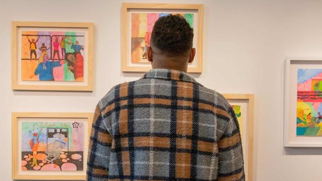 Photo of the back of a person looking at a wall of paintings