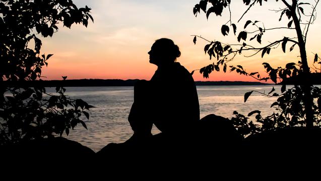 Person in silhouette with orange sky and blue water  