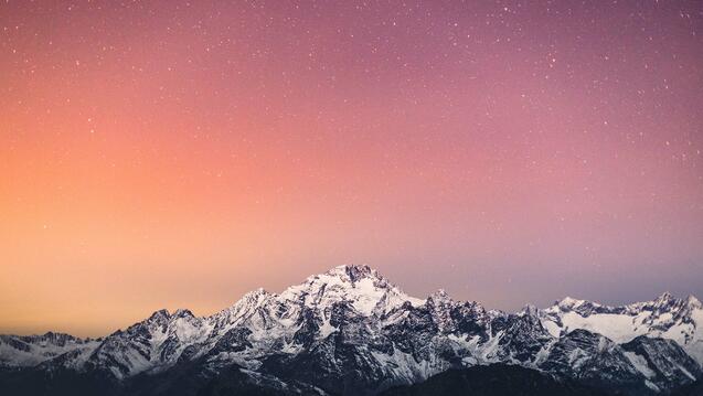 Photo of a snow covered mountain with an orange and pink sky with stars