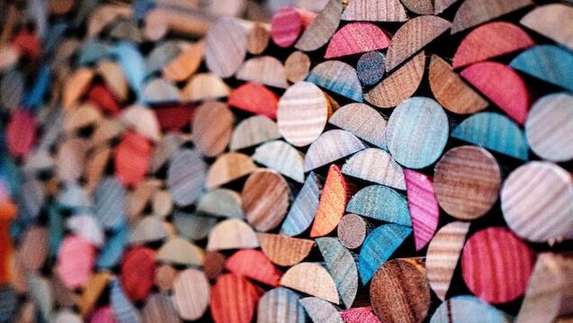 This image showcases a close-up view of a colorful arrangement of wooden shapes, predominantly circles and semicircles, with a variety of vibrant colors like blue, red, orange, and natural wood tones. The textures of the wood grain are visible, adding depth and detail to the composition, which has an abstract, mosaic-like aesthetic.