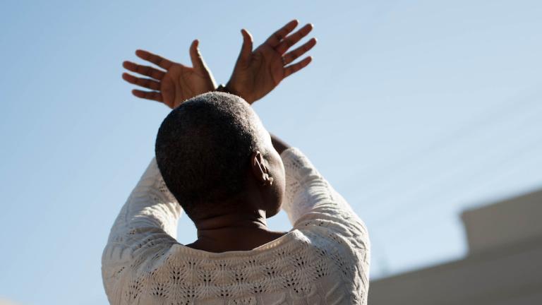 Behind view of person holding their arms above their head with the hands crossed.