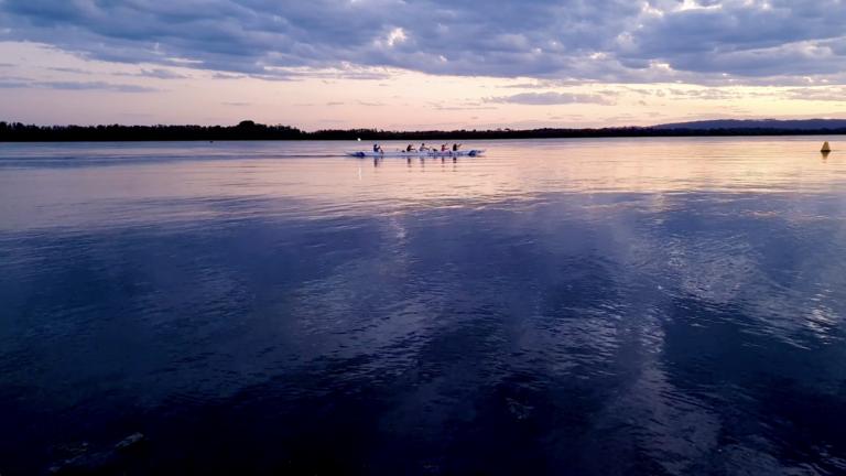 people rowing on a lake with deep blue hues and cloud reflections