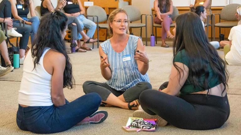 Photo of three women sitting on a floor in discussion