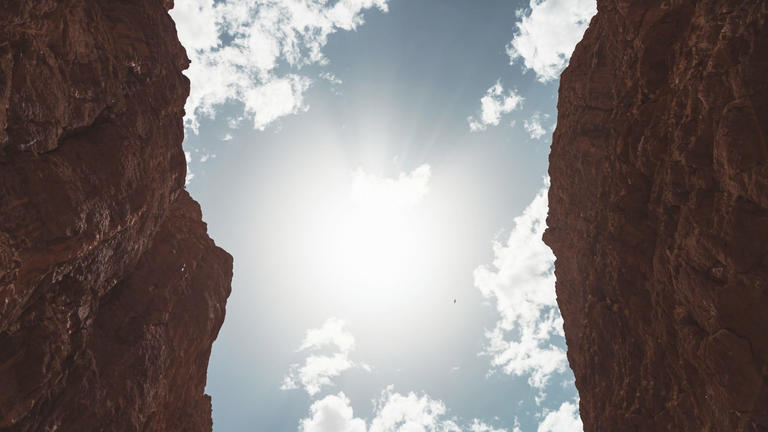 Photo of a blue sky with clouds framed between rocky cliffs by Carouri Hicham on Unsplash