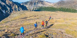 Photo of five people hiking across a sunny meadow surrounded by mountains by Greg Rosenke on Unsplash