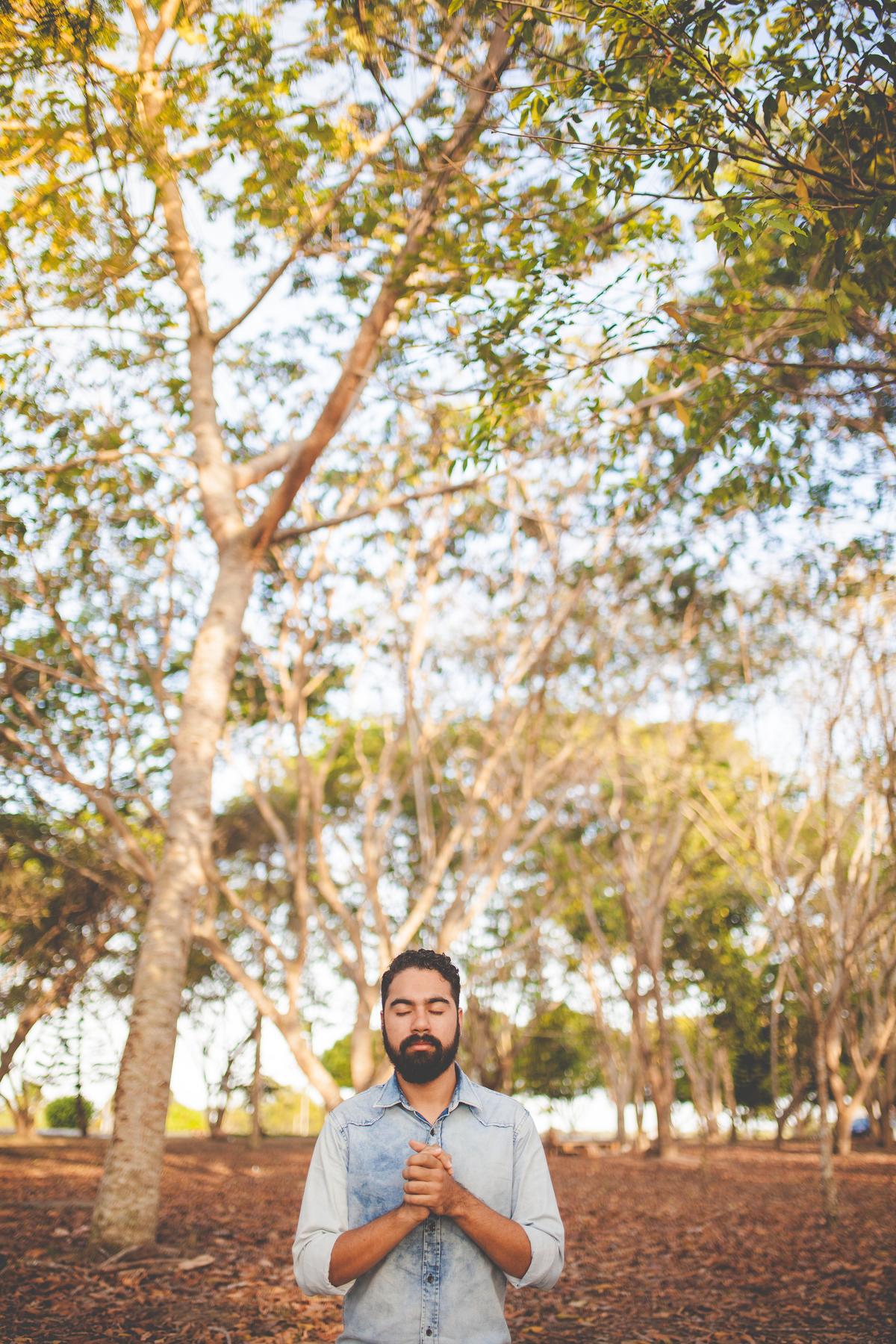 Person with eyes closed and hands over heart in front of a tree