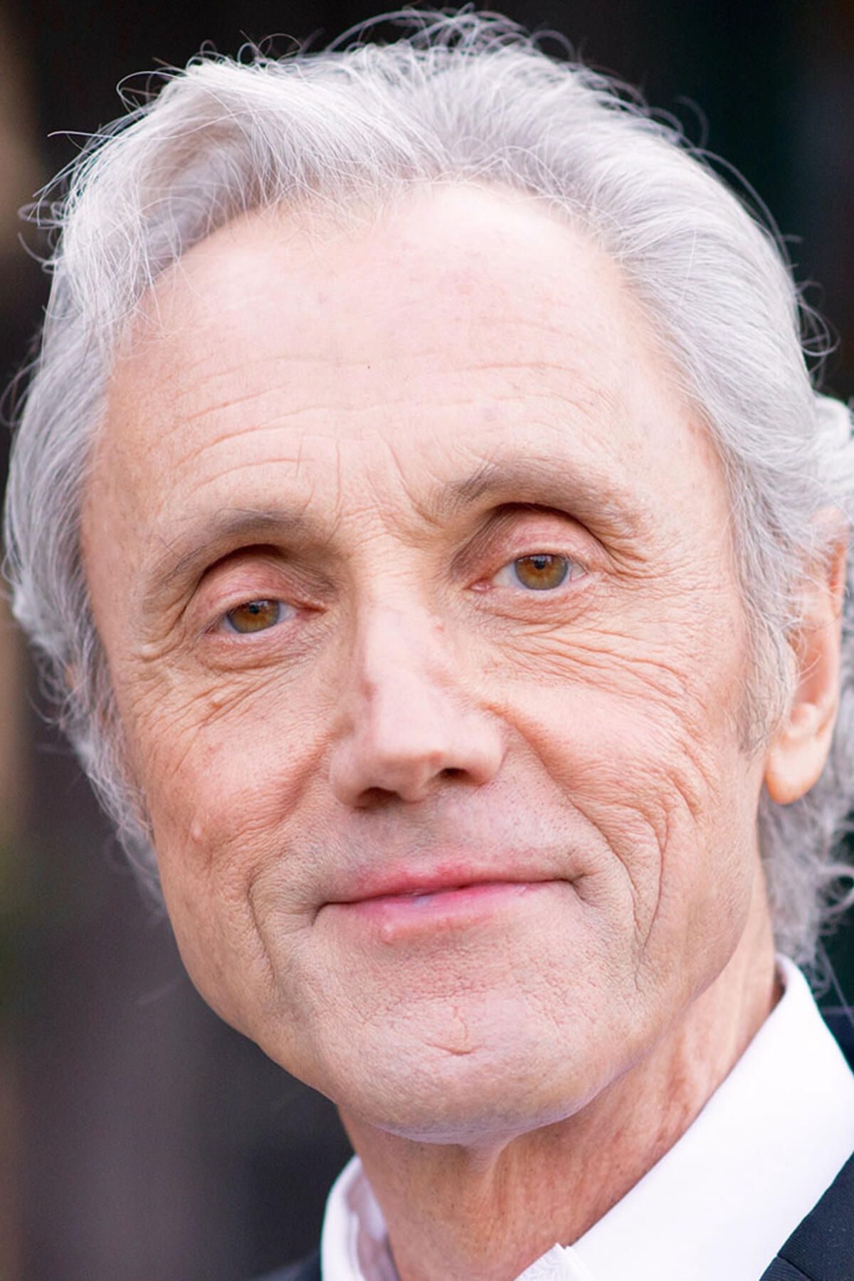 Richard Tarnas color portrait. Richard is an older, white man with short white/silver hair. He is smiling in this portrait and posed in front of a blurred background.